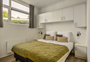 Chambre avec lit double, couvre-lit vert, armoires blanches et grandes fenêtres à Module Special 4 personen.
