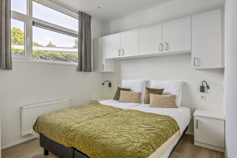 Bedroom with double bed, green bedspread, white cabinets, and large windows at Module Special 4 Personen.