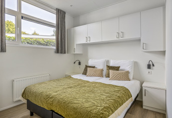 Chambre avec lit double, couvre-lit vert, armoires blanches et grandes fenêtres à Module Special 4 personen.