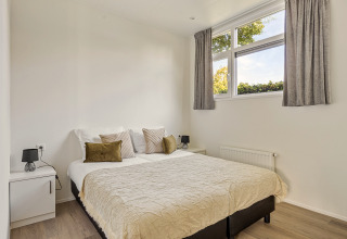 Chambre lumineuse avec lit double, murs blancs et grandes fenêtres dans une lodge à Recreatiepark het Esmeer.