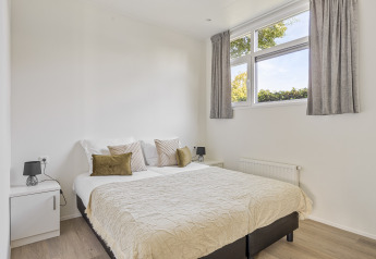 Bright bedroom with double bed, white decor, large windows and curtains at Recreatiepark het Esmeer lodge.