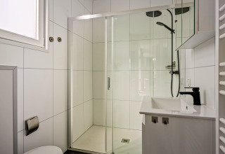 Salle de bain moderne avec douche, carrelage blanc, robinet noir et fenêtre dans le Module Special 4 personen.