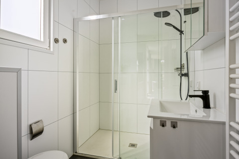 Bagno moderno con doccia, piastrelle bianche, rubinetto nero e finestra nel lodge Module Special 4 personen.