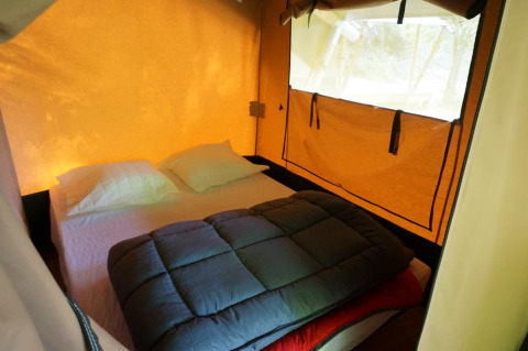 Interieur van de Baroudeur safaritent met dubbel bed, kussens en raam bij Bivouac nature in Frankrijk.