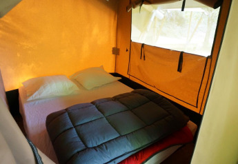 Interno della tenda safari Baroudeur con letto matrimoniale, cuscini e finestra a Bivouac nature in Francia.