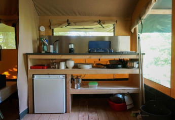 Angolo cucina nella tenda Baroudeur con fornello a gas, mini frigo, utensili e scaffali in legno.