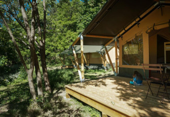 Safari telt ved Bivouac nature i Frankrig omgivet af træer med et barn siddende på terrassen i solen.