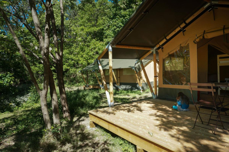 Baroudeur safari tent at Bivouac nature in France, surrounded by trees, with a child sitting on the deck.