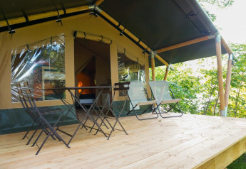 Træterrasse med borde og stole foran Baroudeur Safari-teltet på Bivouac nature i Frankrig.