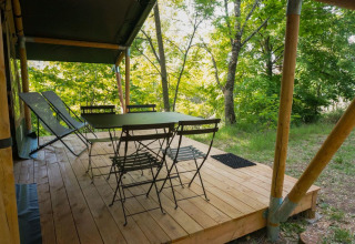 Terrasse en bois de la tente safari Baroudeur avec table, chaises et transats dans un cadre forestier.