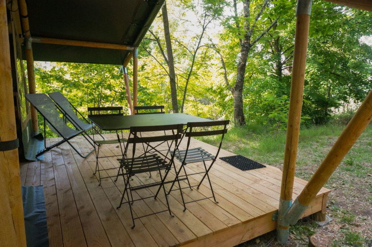 Houten terras van de Baroudeur safaritent met klapstoelen, tafel en ligzetels in een groene natuur.