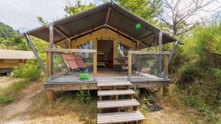 Safari Baroudeur-telt med træterrasse, liggestole og naturskøn udsigt, omgivet af grøn vegetation.