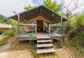 Safari Baroudeur-telt med træterrasse, liggestole og naturskøn udsigt, omgivet af grøn vegetation.