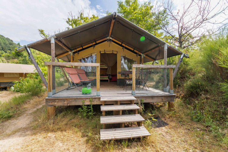 Baroudeur safaritent met houten terras en ligstoelen, omringd door weelderige groene vegetatie en natuur.