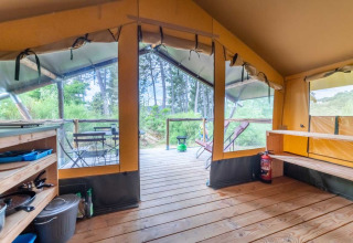 Intérieur d'une tente Baroudeur à Bivouac nature en France, vue sur la terrasse en bois et la végétation.