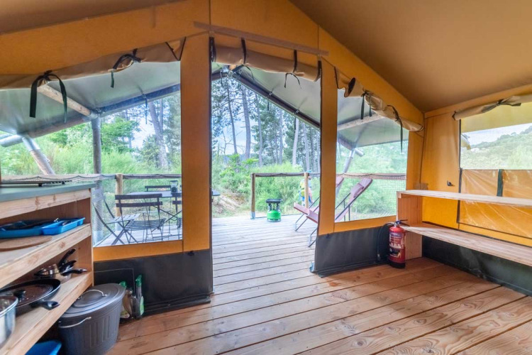 Interno della tenda Baroudeur al Bivouac nature in Francia, con terrazza in legno e vista sulla natura.