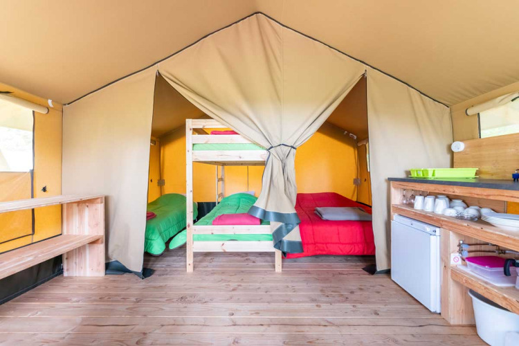 Interior de la tienda Baroudeur en Bivouac Nature, Francia, con literas, cama doble y cocina básica.