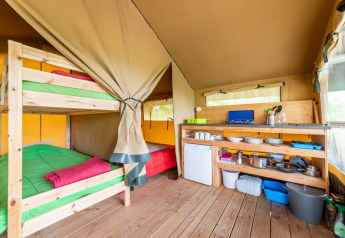 Interior de la tienda safari Baroudeur con literas y cocina en Bivouac Nature, Francia.