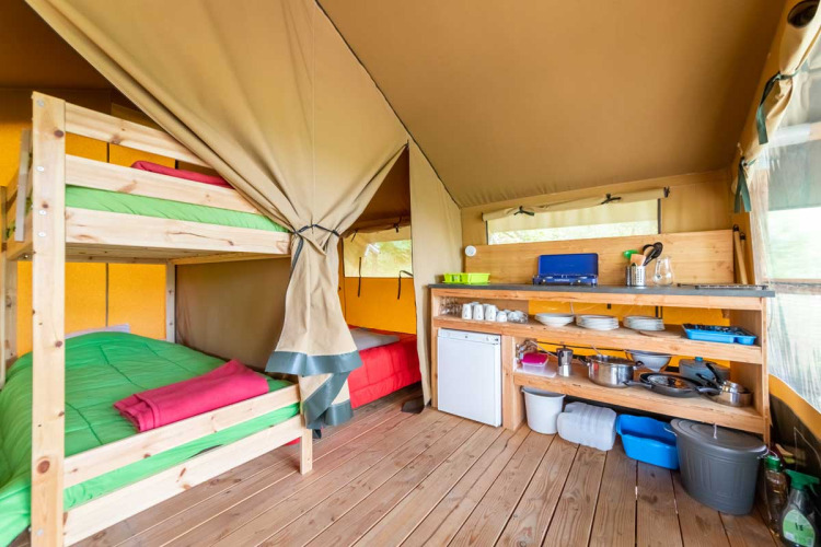 Interior de la tienda safari Baroudeur con literas y cocina en Bivouac Nature, Francia.