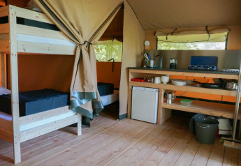 Interno della tenda safari Baroudeur al Bivouac nature in Francia, con cucina e letti a castello.