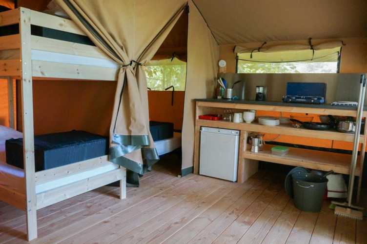 Interior de la tienda safari Baroudeur en Bivouac nature, Francia, con cocina y literas de madera.