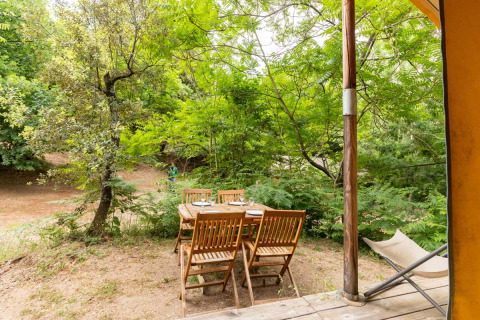 Outdoor wooden dining set beside the Canadienne Tent at Bivouac nature in France, surrounded by trees.