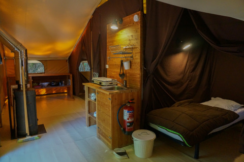 Indvendigt billede af en hyggelig safari-telt ‘Canadienne’ på Bivouac nature i Frankrig med seng og køkken.