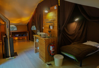 Interior view of cozy ‘Canadienne’ safari tent at Bivouac nature in France with bed, kitchenette and stove.