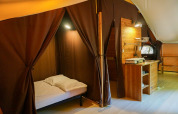 Interno della tenda safari «Canadienne» al Bivouac nature in Francia, con letto, mobili e tende.