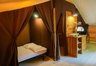 Intérieur de la tente safari «Canadienne» au Bivouac nature en France, avec lit, meubles et rideaux.