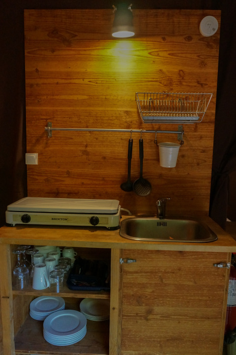 Pequeña cocina con fregadero, placa caliente y utensilios en una tienda safari en Bivouac Nature, Francia.