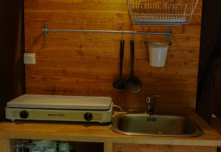 Pequeña cocina con fregadero, placa caliente y utensilios en una tienda safari en Bivouac Nature, Francia.