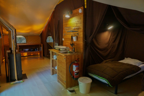 Interieur van Canadienne safaritent met houtkachel, bed en keuken bij Bivouac nature in Frankrijk.