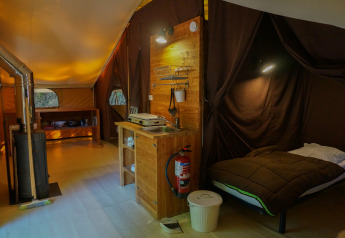 Interieur van een Canadienne safaritent met houtkachel, bed en keuken bij Bivouac nature in Frankrijk.