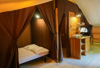 Binnenaanzicht van de «Canadienne» safaritent bij Bivouac nature in Frankrijk, met bed en houten keuken.