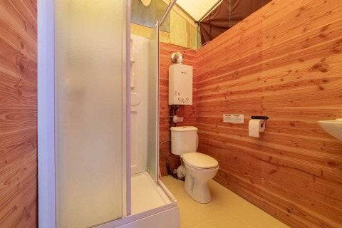 Salle de bain dans une tente safari Canadienne avec murs en bois, douche et toilettes à Bivouac Nature, France.