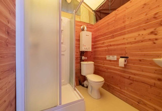 Badeværelse i en Canadienne safari-telt med træbeklædte vægge, brusekabine og toilet ved Bivouac Nature i Frankrig.