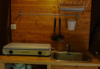 Kleine keuken in safaritent met houten panelen, gootsteen, kookplaat en servies bij Bivouac nature in Frankrijk.