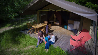 Familie nyder tid foran et safari telt med træterrasse, spisebord, stole og afslappende omgivelser.