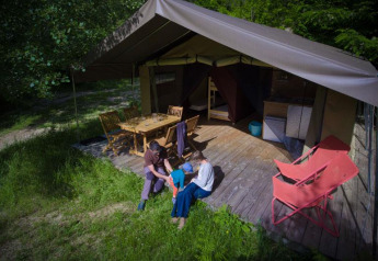 Famiglia si rilassa davanti a una tenda safari con terrazza in legno, tavolo, sedie e prato verde.