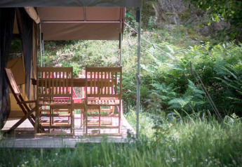 Houten stoelen en tafel op het terras van een safaritent bij Bivouac nature, omgeven door natuur in Frankrijk.