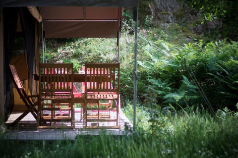 Sedie e tavolo in legno sulla veranda di una tenda safari al Bivouac nature, circondata dal verde in Francia.