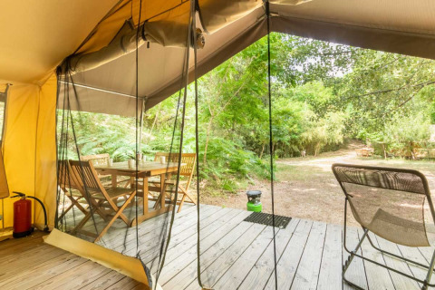 Vista dalla tenda safari a Bivouac nature, Francia, con terrazza in legno, tavolo, sedie e verde naturale.