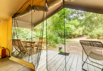 Vista dalla tenda safari a Bivouac nature, Francia, con terrazza in legno, tavolo, sedie e verde naturale.