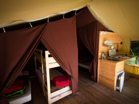 Interno di tenda safari con letti a castello, zona notte e angolo cottura presso Bivouac Nature, Francia.