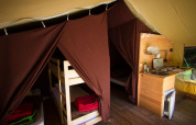 Interno di tenda safari con letti a castello, zona notte e angolo cottura presso Bivouac Nature, Francia.