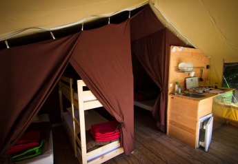 Interno di tenda safari con letti a castello, zona notte e angolo cottura presso Bivouac Nature, Francia.
