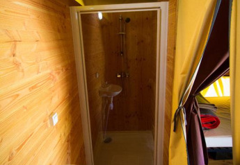 Baño con ducha y lavabo dentro de una tienda safari en Bivouac nature, Francia, con paredes de madera.