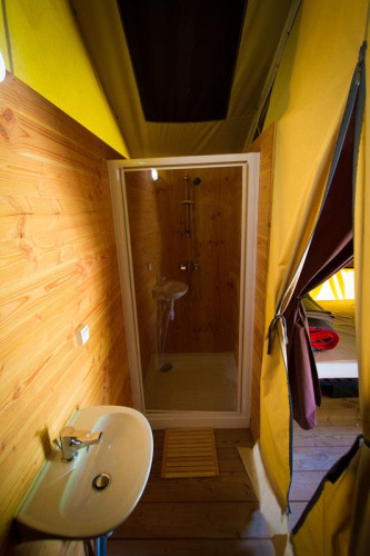 Bathroom with shower and sink inside a safari tent at Bivouac nature in France, decorated with wood walls.