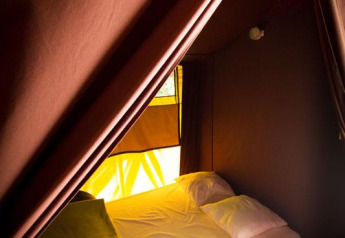 Interno di una tenda safari con letto, cuscini e coperte al Bivouac nature in Francia.
